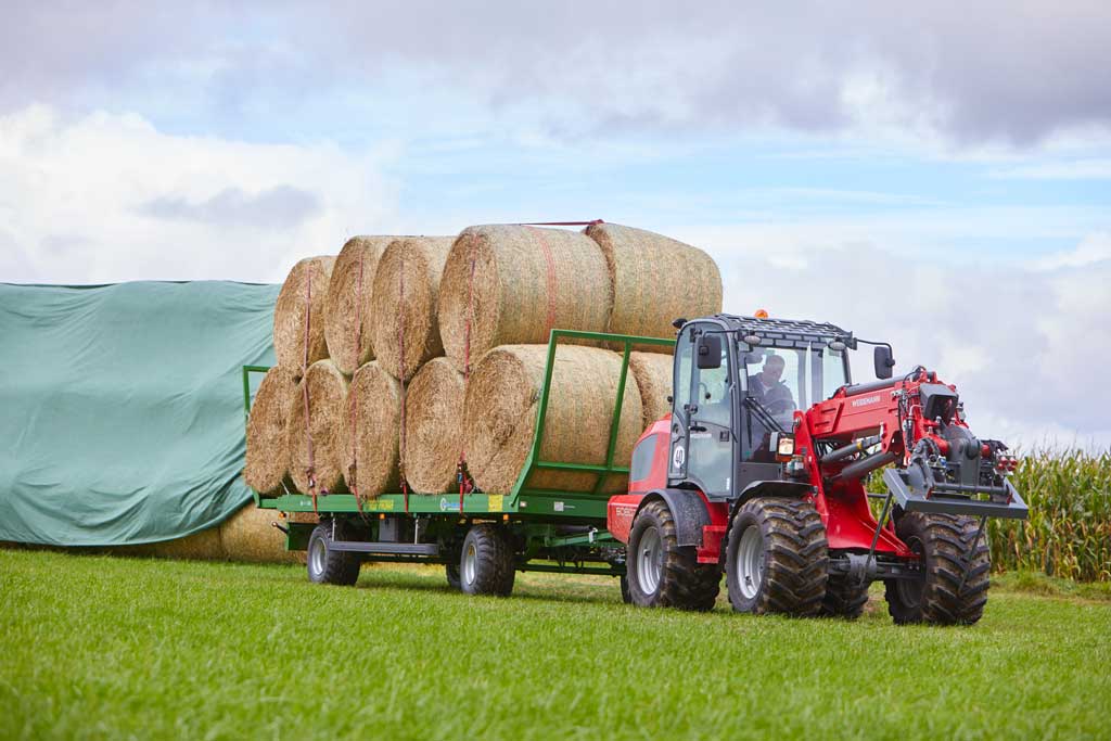 Weidemann wheel loader towing trailer loaded with round hay bales in agricultural field – ideal for farm transport and bale handling.