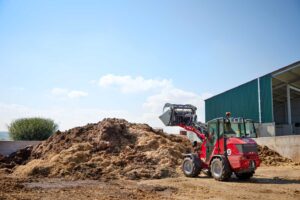 Weidemann 1260LP compact wheel loader moving manure on a farm job site with high pile handling attachment.