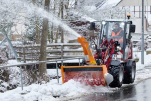 Weidemann 1390 compact wheel loader with snow blower attachment clearing snow from a road in winter.