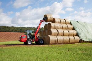 Weidemann 3080T telescopic wheel loader stacking large round hay bales in a field, perfect for hay and livestock management.