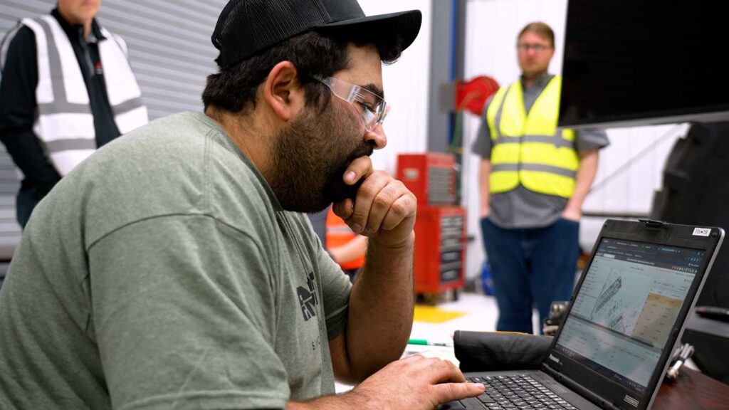 Cody uses laptop with judges onlooking in background