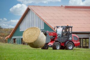 Weidemann 2080LPT loader transporting a large round hay bale across a farm field in front of