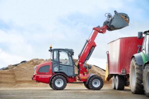 Weidemann 2080LPT telescopic wheel loader lifting and dumping material into a feed mixer on a livestock farm.