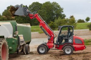 Weidemann 2080T telescopic wheel loader unloading silage into a feed mixer, showcasing high lift capacity and precision in agricultural applications.