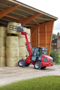 Weidemann 2080T wheel loader lifting round hay bales into storage, demonstrating excellent reach and handling for hay and cattle operations.