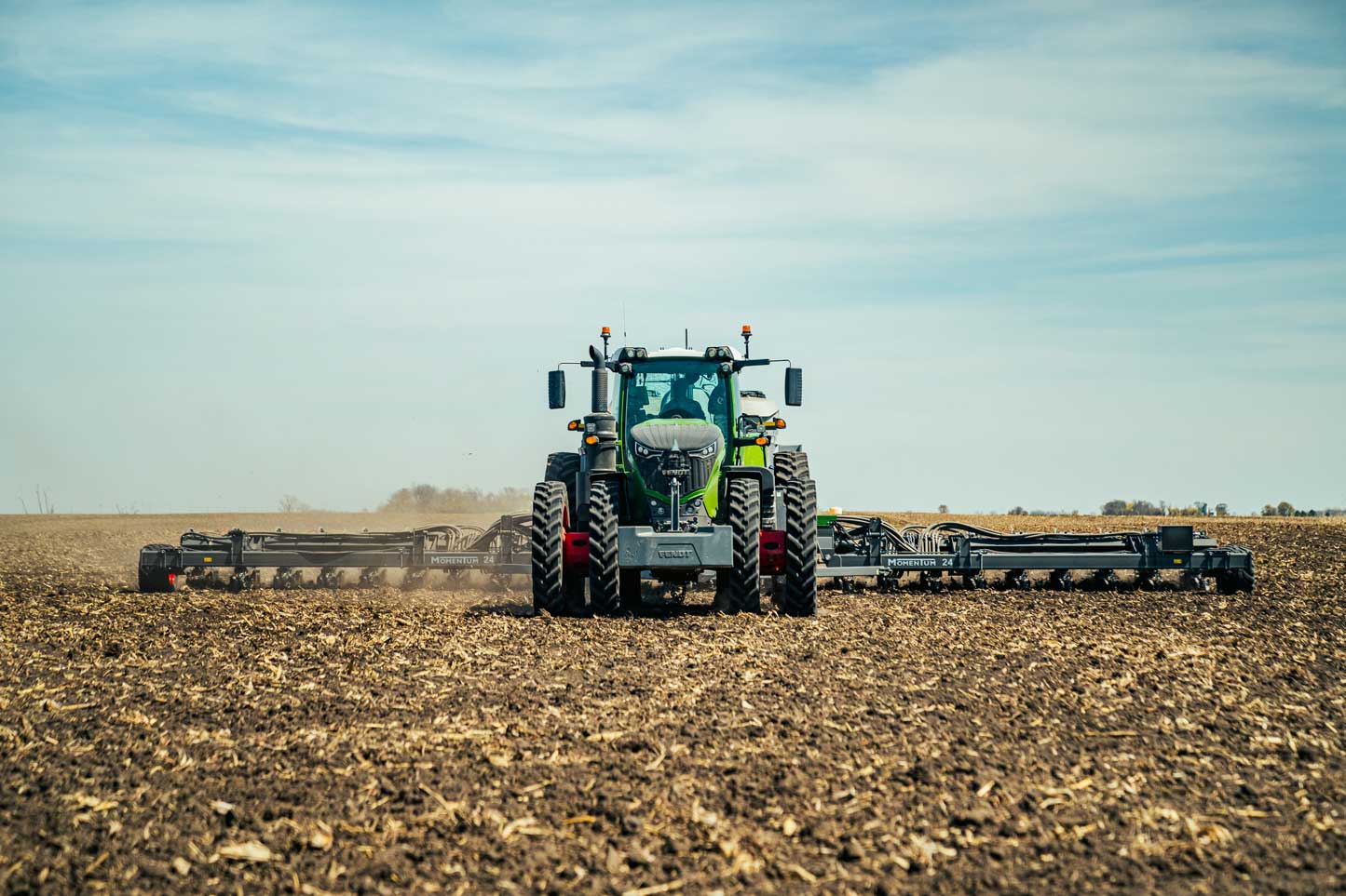 Front view of a Fendt 1000 Vario tractor working in a field, pulling a wide tillage implement under a clear sky.