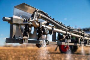Close-up of Fendt Rogator 900 sprayer nozzles in action, showcasing precision spraying technology against a bright blue sky in a field setting, designed for efficient and accurate agricultural application.