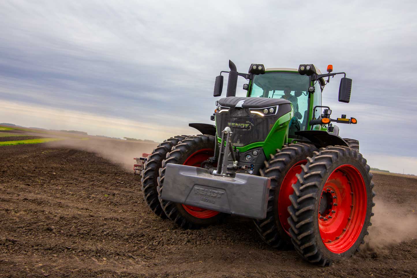 Fendt 1042 Vario tractor with front weight, pulling a Sunflower 6830 tillage implement across a freshly worked field under a cloudy sky.