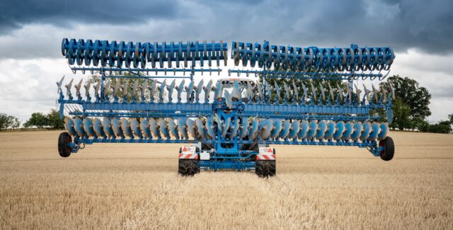 Rear view of a LEMKEN Rubin 10 compact disc harrow operating in a harvested wheat field, featuring its symmetrical disc arrangement and wide working width under a dramatic sky.