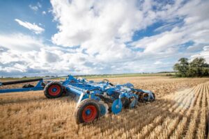 Lemken Rubin 10 2024 high-speed disc harrow working in a harvested wheat field under a partly cloudy sky, showcasing its wide working width and heavy-duty build.