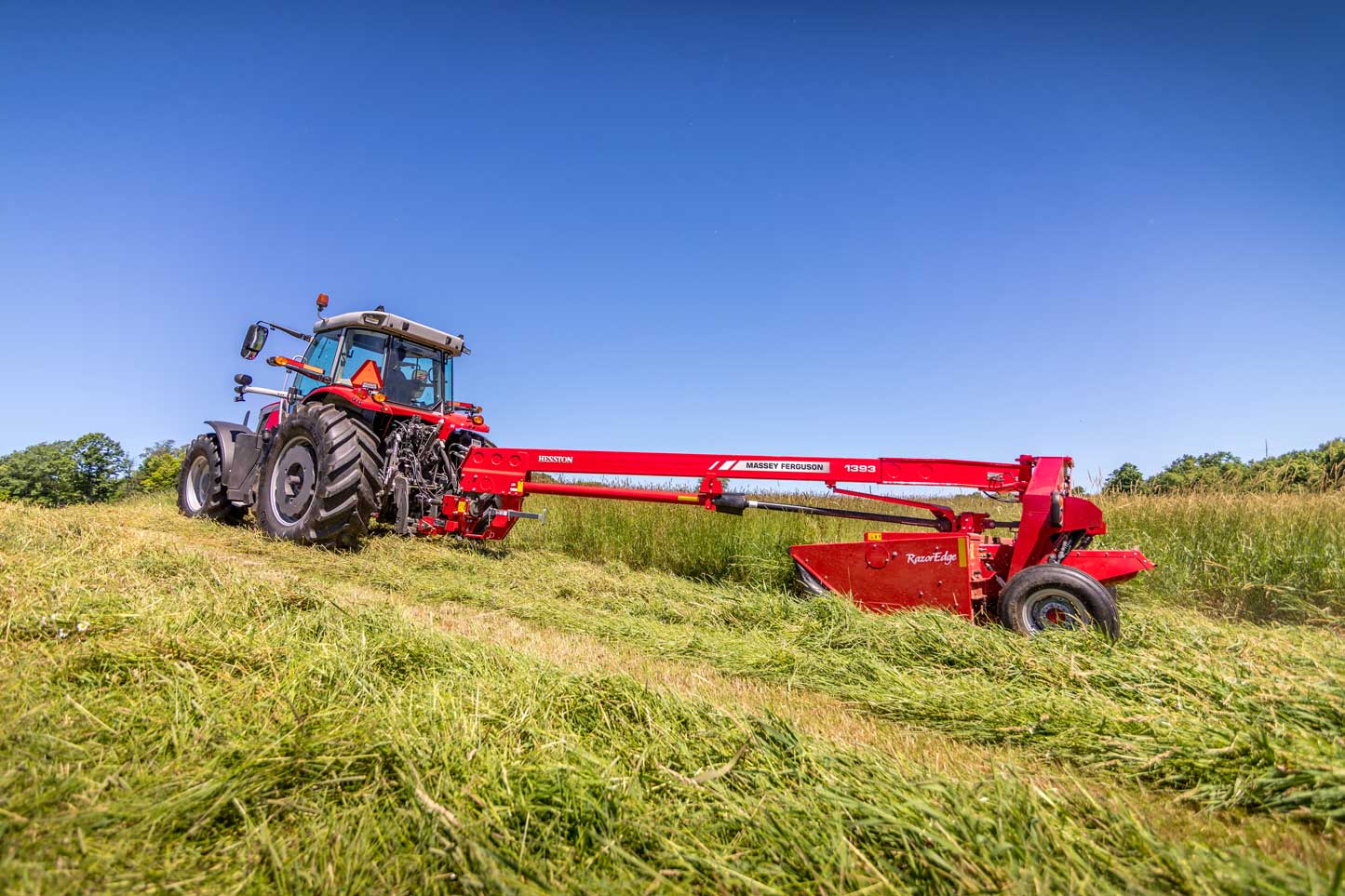 Massey Ferguson 1393 disc mower conditioner with RazorEdge cutterbar pulled by a tractor cutting thick hay in a southern Alberta field under clear blue sky.