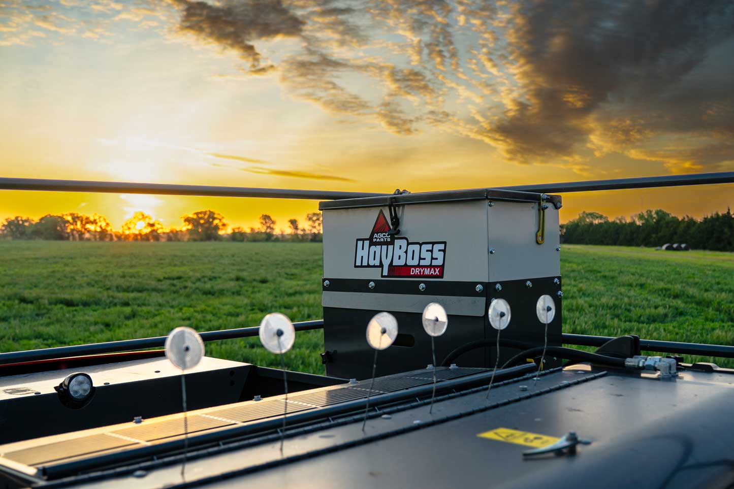 HayBoss DryMax hay preservative applicator mounted on a baler at sunrise in a southern Alberta hay field, Hanlon Ag Centre Lethbridge farm equipment dealership.
