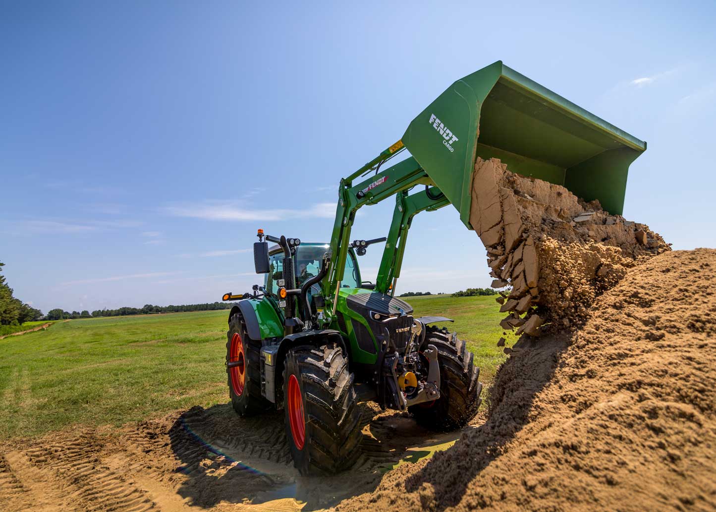 Fendt 600 front loader tractor working in a field, moving soil under clear blue sky.