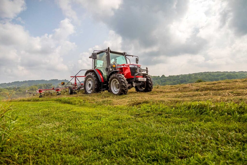 Massey Ferguson MF4700 tractor raking hay in a green field, showing a reliable haying setup used for forage management.