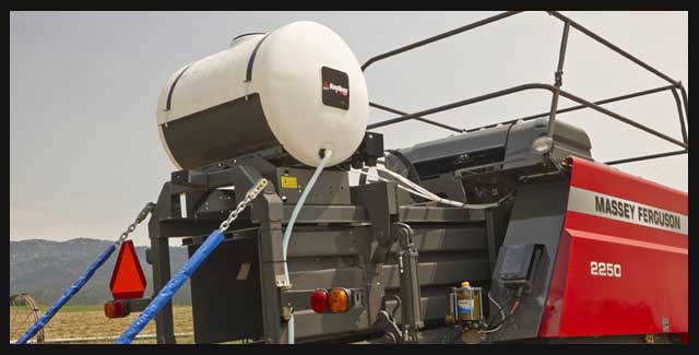 Preservative applicator (Hayboss) mounted on top of a large square baler, designed to improve hay quality and reduce spoilage, shown on forage equipment available at Hanlon Ag Centre in southern Alberta for Prairie hay producers. Demonstrating AGCO parts available at Hanlon Ag Centre.