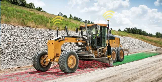 A yellow motor grader fitted with Trimble grade-control antennas smoothing a gravel road, with wireless signal icons and guidance overlays illustrating RTK positioning